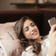 Woman in White Top Holding Smartphone Lying on Couch